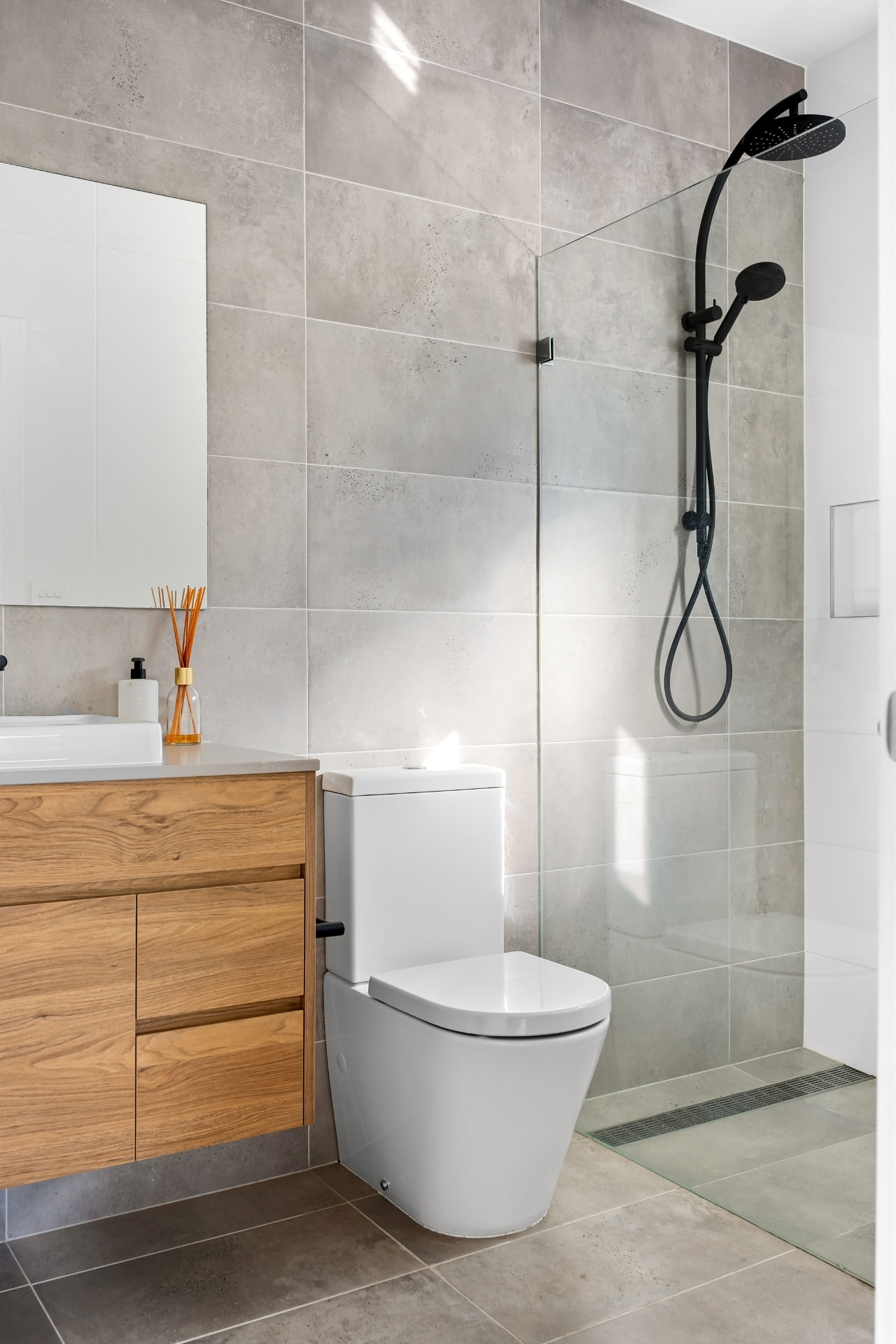 Bright bathroom with floating oak vanity, concrete-look tile and a glass walk-in shower