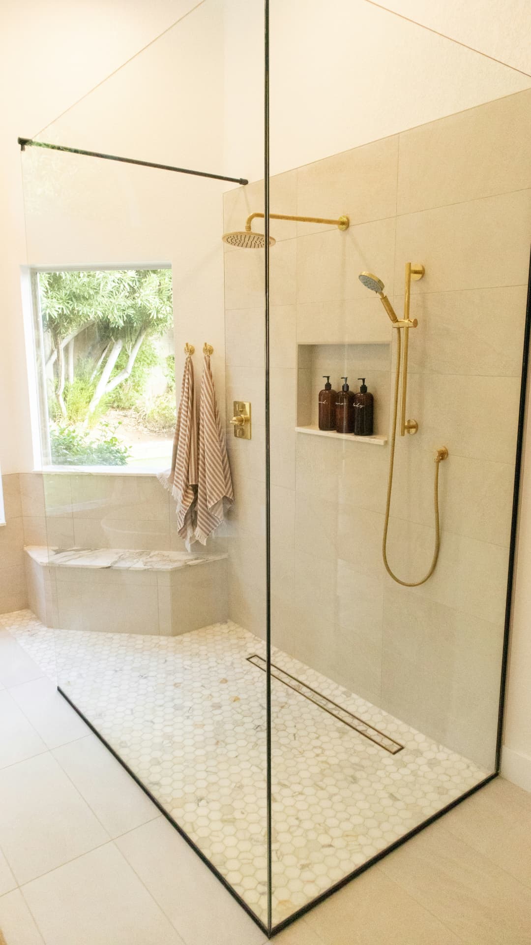 Curbless walk-in shower with frameless glass, limestone tile and brushed brass fixtures